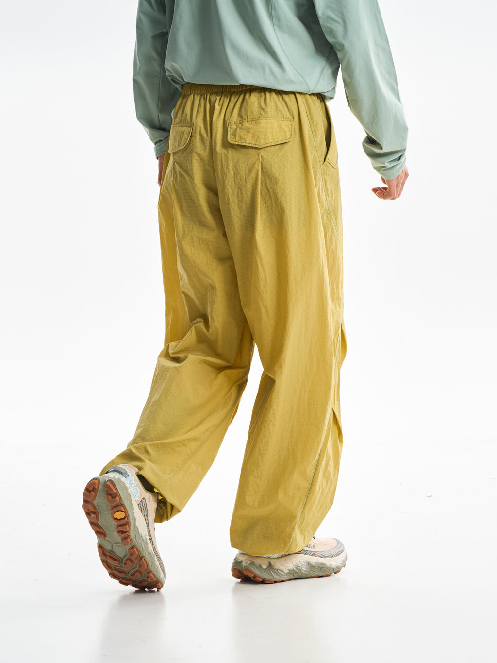 Yellow hiking pants — rear three-quarter stride showing the pocket and raised heel