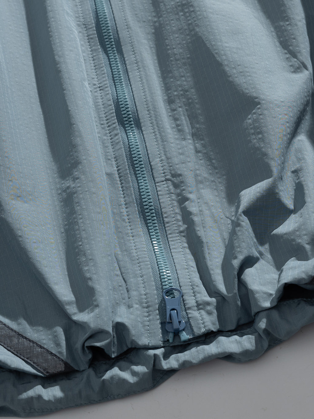 Blue jacket — lower front zip, slider and gathered edge detail