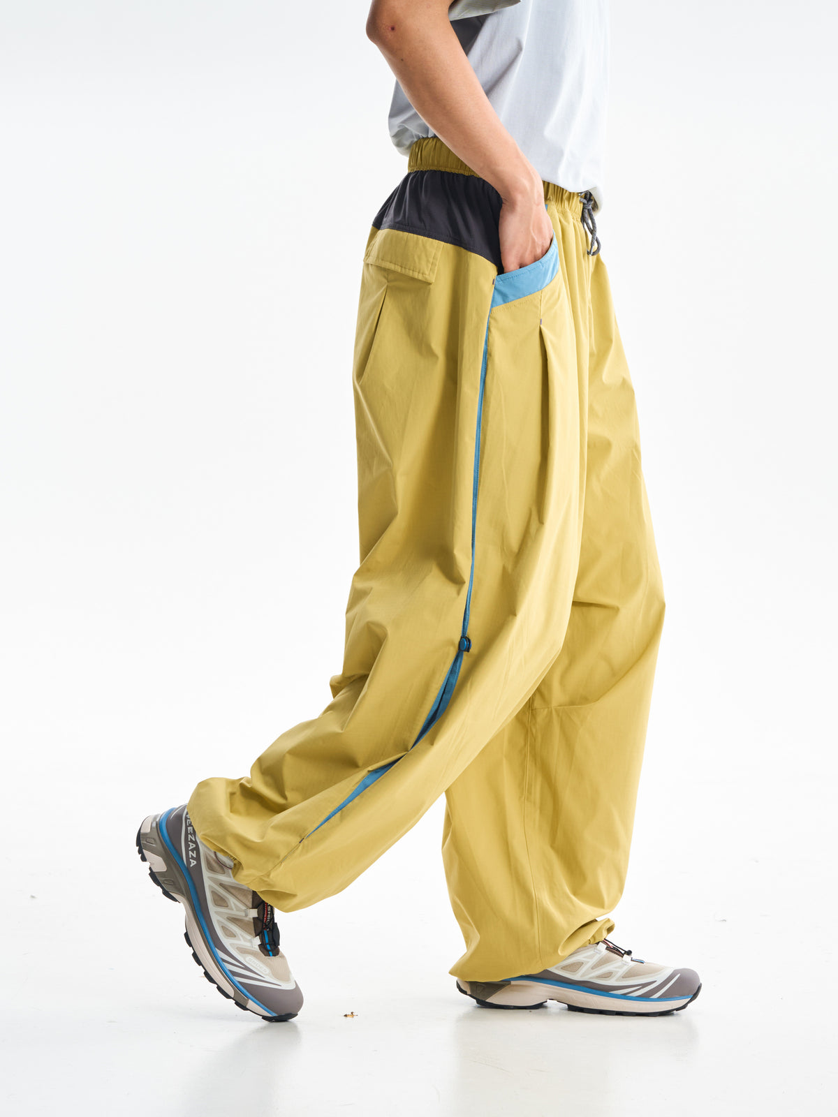 Yellow hiking pants — walking side view showing the blue panel and side snaps